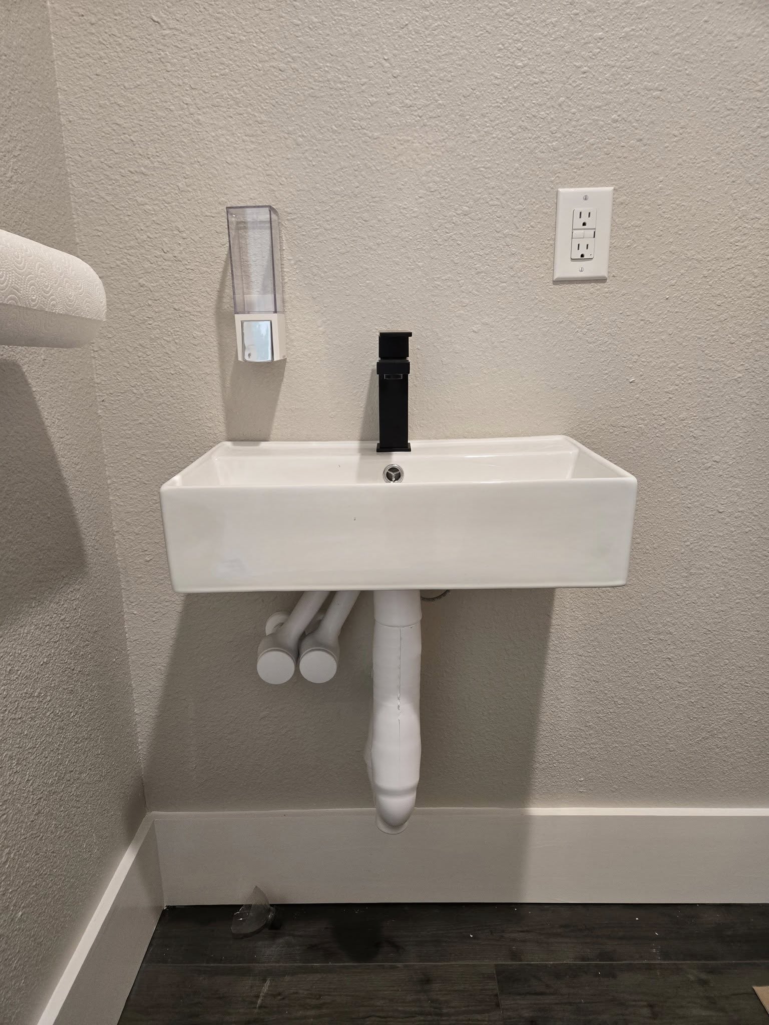 Wall-mounted commercial sink installed with black faucet and exposed drain and supply connections