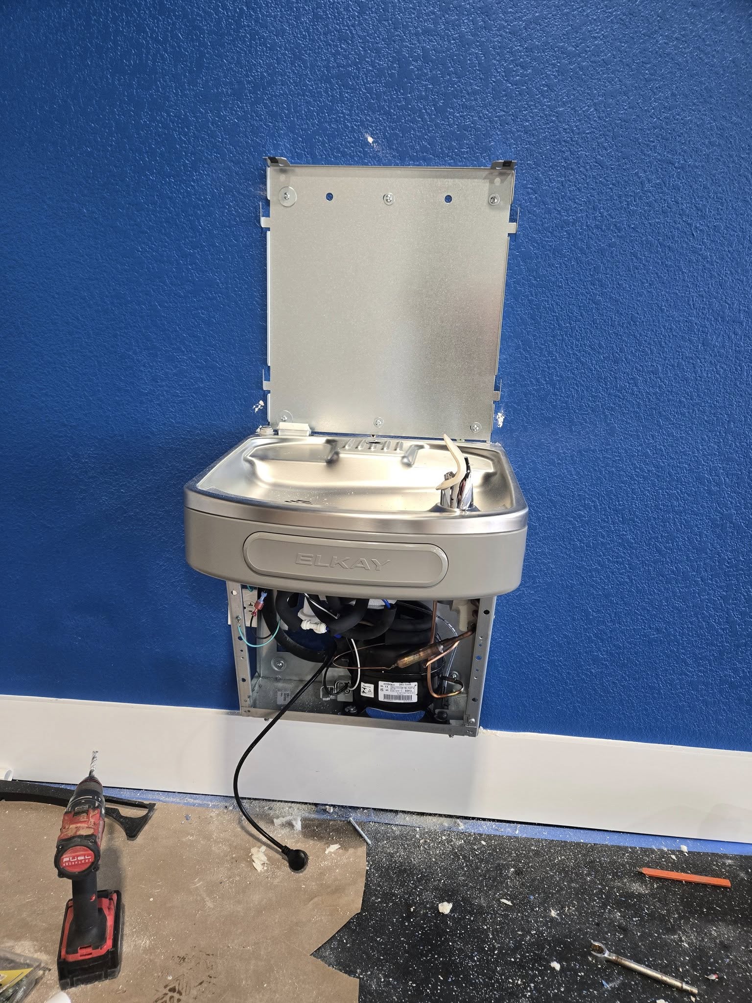 Wall-mounted Elkay drinking fountain during installation with the front access panel open.