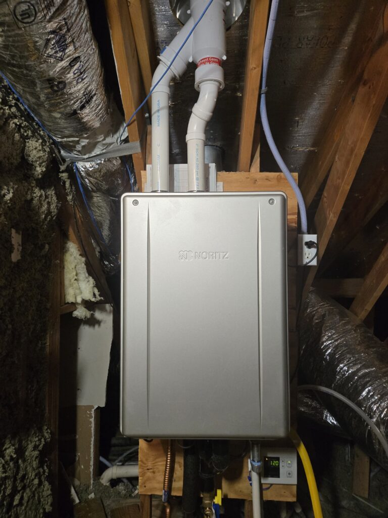 Noritz tankless water heater installed in an attic space with venting and water line connections.